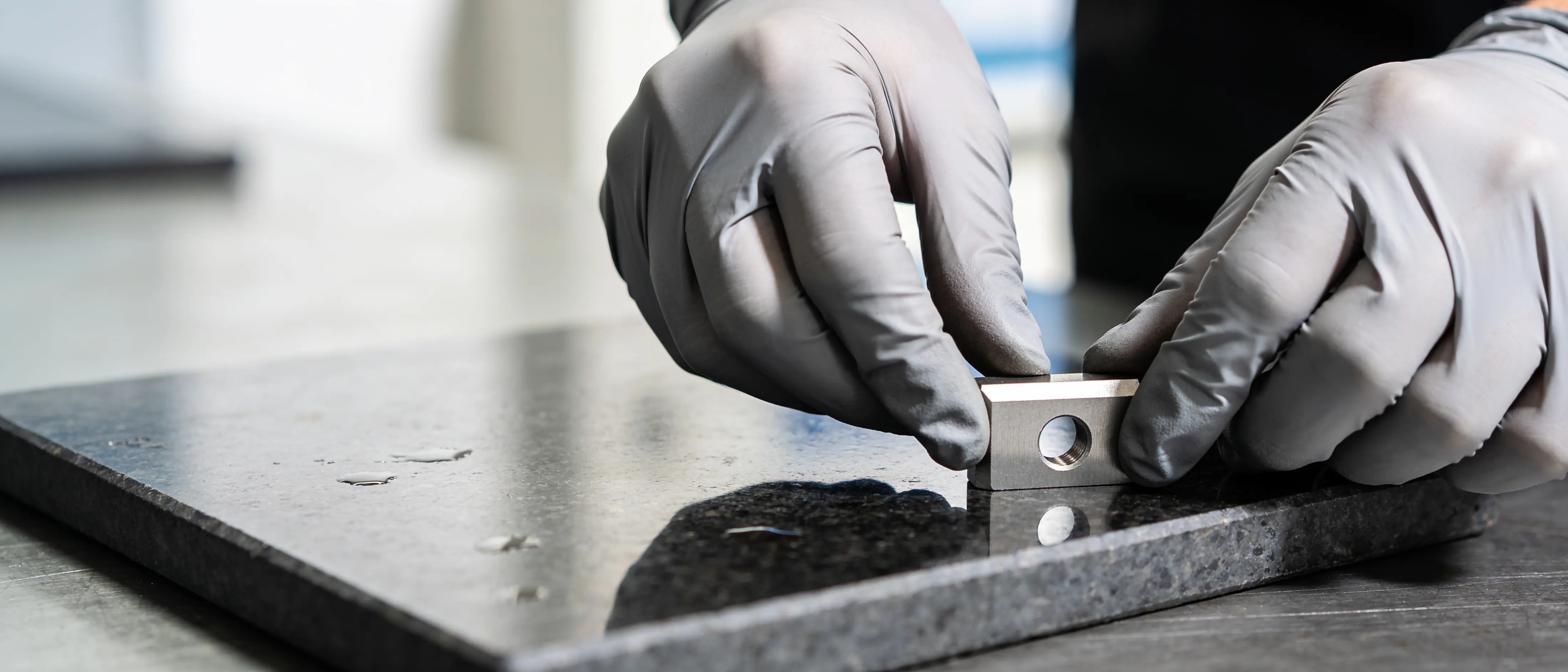 Hände mit Handschuhen legen ein Stanzteil auf eine Messplatte aus Granit
